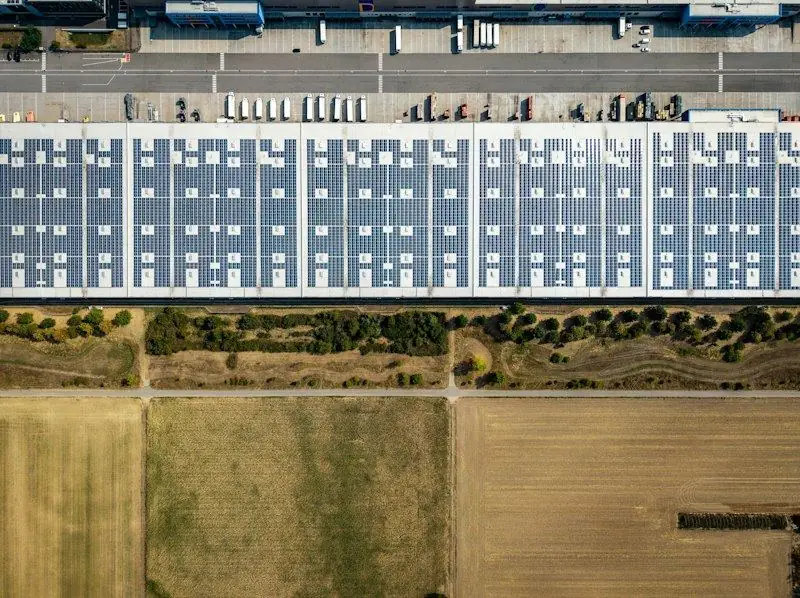 An industrial building with solar panels surrounded by fields